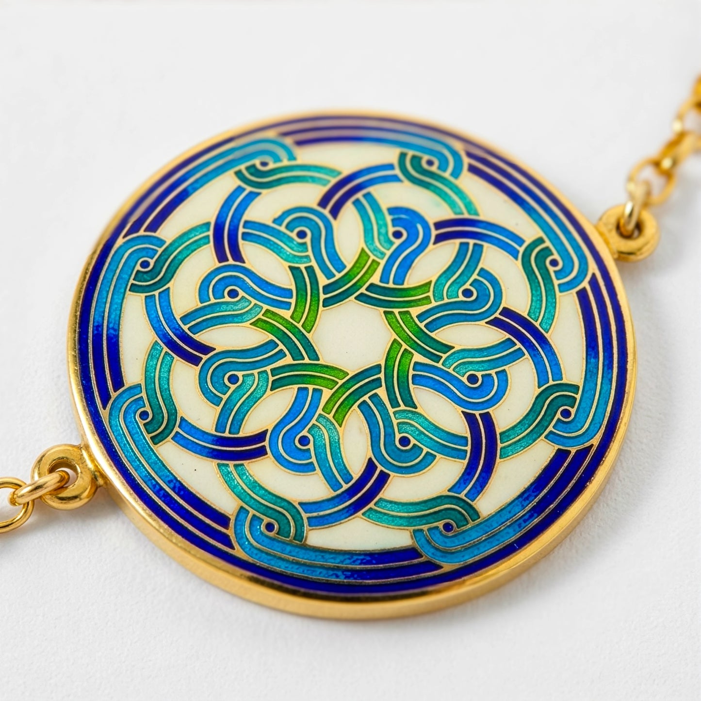Decorative pendant with intricate blue and green patterns on a gold chain against a white background